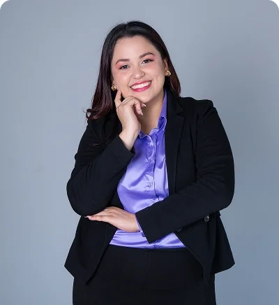 Retrato de Andrea Paz, mentora de Be MEE, con blazer negro y blusa satinada lila, sonriendo y posando frente a un fondo gris