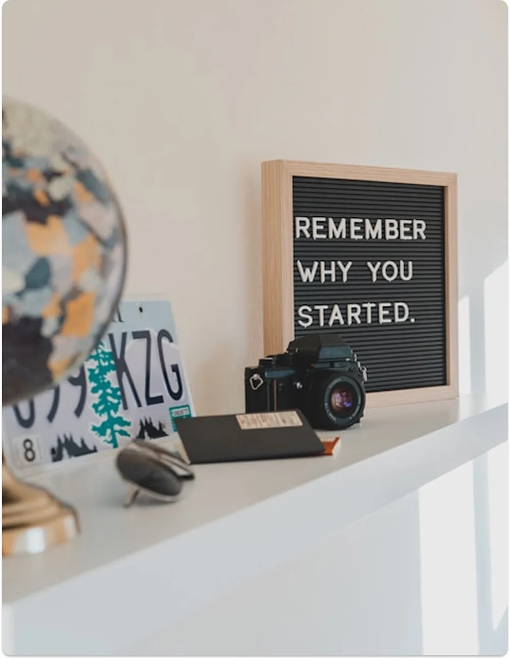 Escritorio con cartel que dice “Remember why you started”, cámara y globo terráqueo, simbolizando motivación e inspiración en el camino de Be MEE Mentoría.